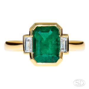 front view of custom-made emerald ring with baguette diamond shoulder