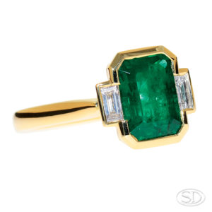 custom made emerald ring with baguette diamond shoulder sitting in a two-third angle